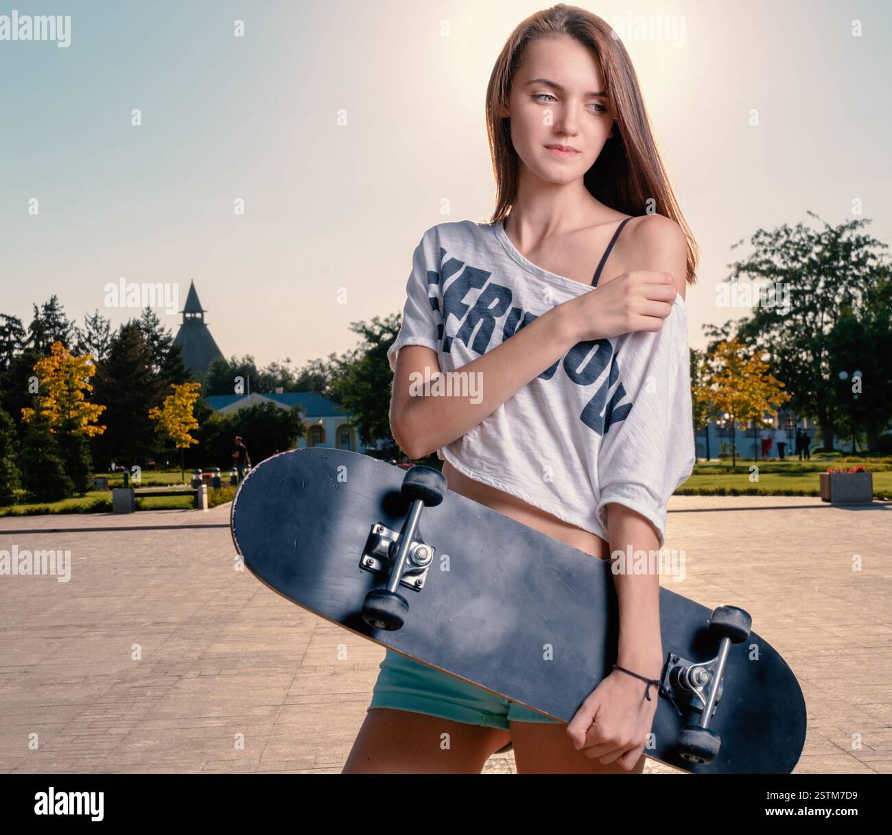 Fille mignonne tenant skateboard posant avec l'épaule nue Banque D'Images