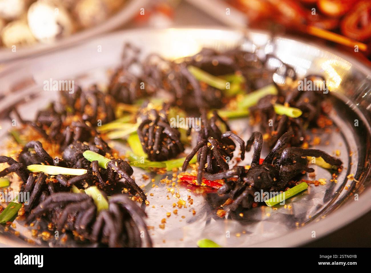 Assiette remplie de tarentules cuites garnies d'herbes vertes et d'épices, offrant une expérience culinaire unique. Banque D'Images