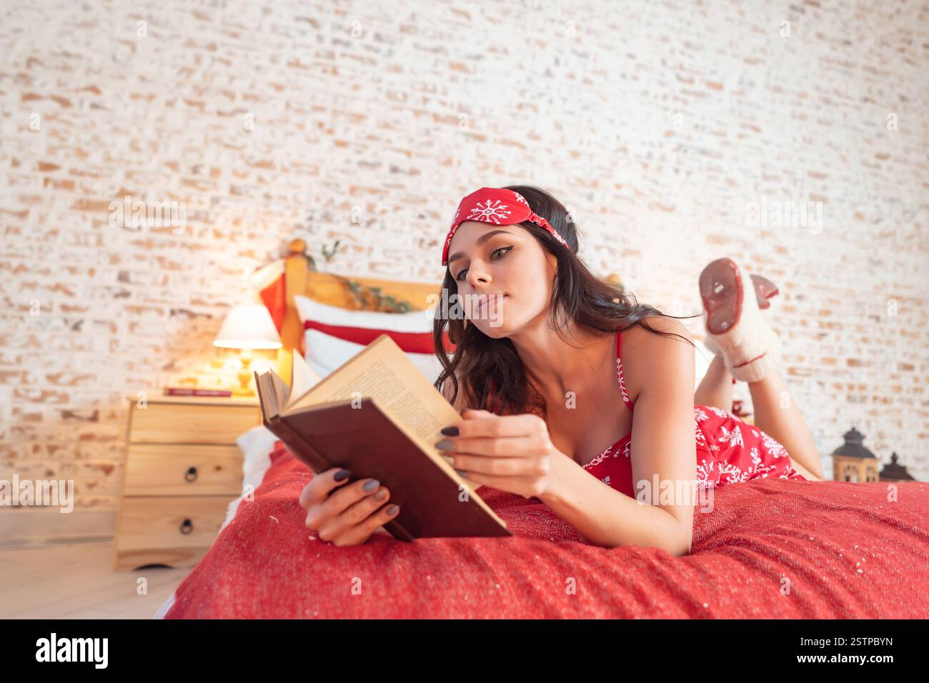 Séduisante femme aux cheveux longs en pyjama rouge reposant sur le lit Banque D'Images