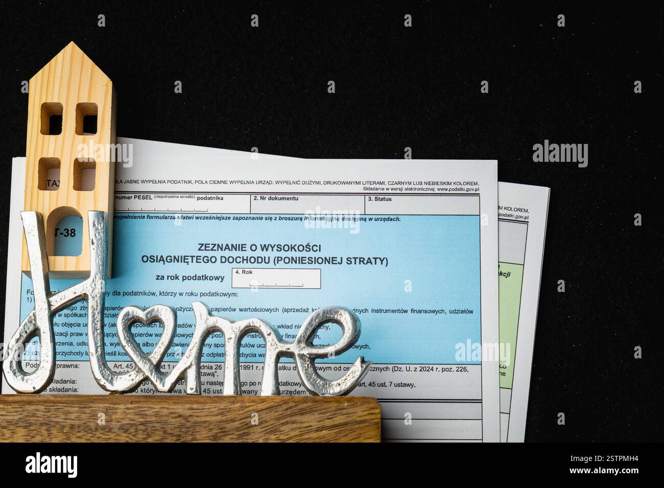 Sur une table se trouvent des formulaires d'impôt polonais à côté d'une charmante maison en bois et une pièce décorative en métal orthographiant amour. Banque D'Images