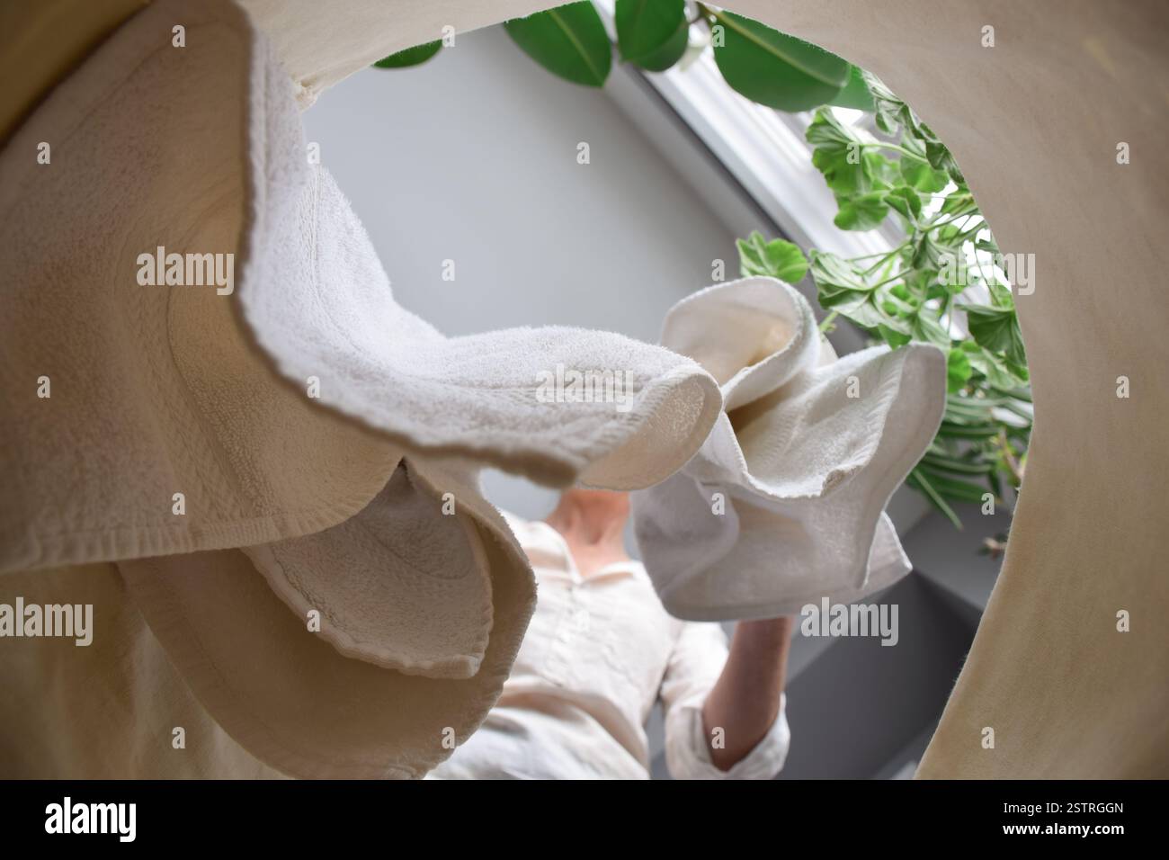 La femme jette des serviettes sales dans le panier à linge, vue de l'intérieur du panier Banque D'Images