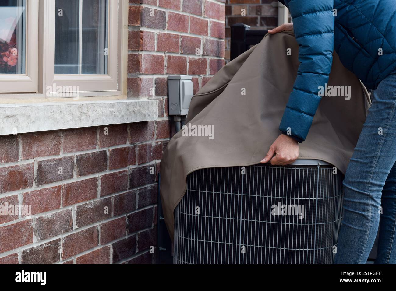 Femme mettant la couverture sur l'unité de climatiseur à l'extérieur de la maison Banque D'Images