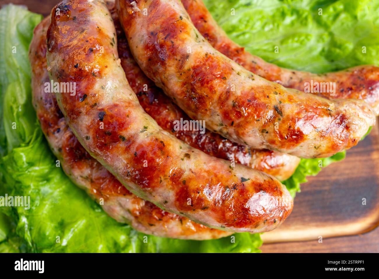 Les saucisses juteuses sont savamment grillées à un brun doré et placées sur des feuilles de laitue vert vif. Le plat offre une présentation alléchante, parfaite pour Banque D'Images