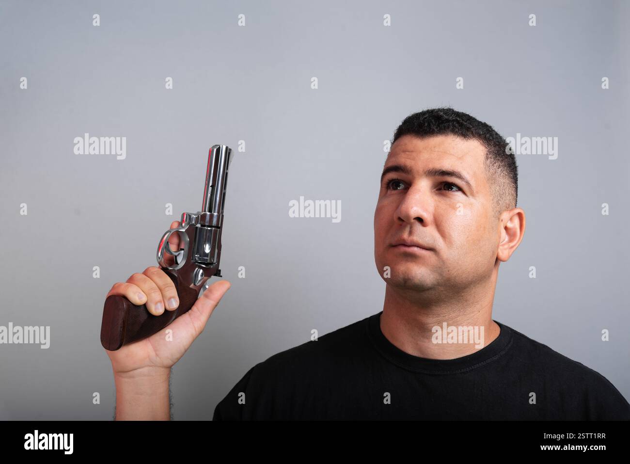 Photo stock d'un bel homme portant une chemise noire et un Jean tenant une arme à feu. isolé sur fond gris Banque D'Images