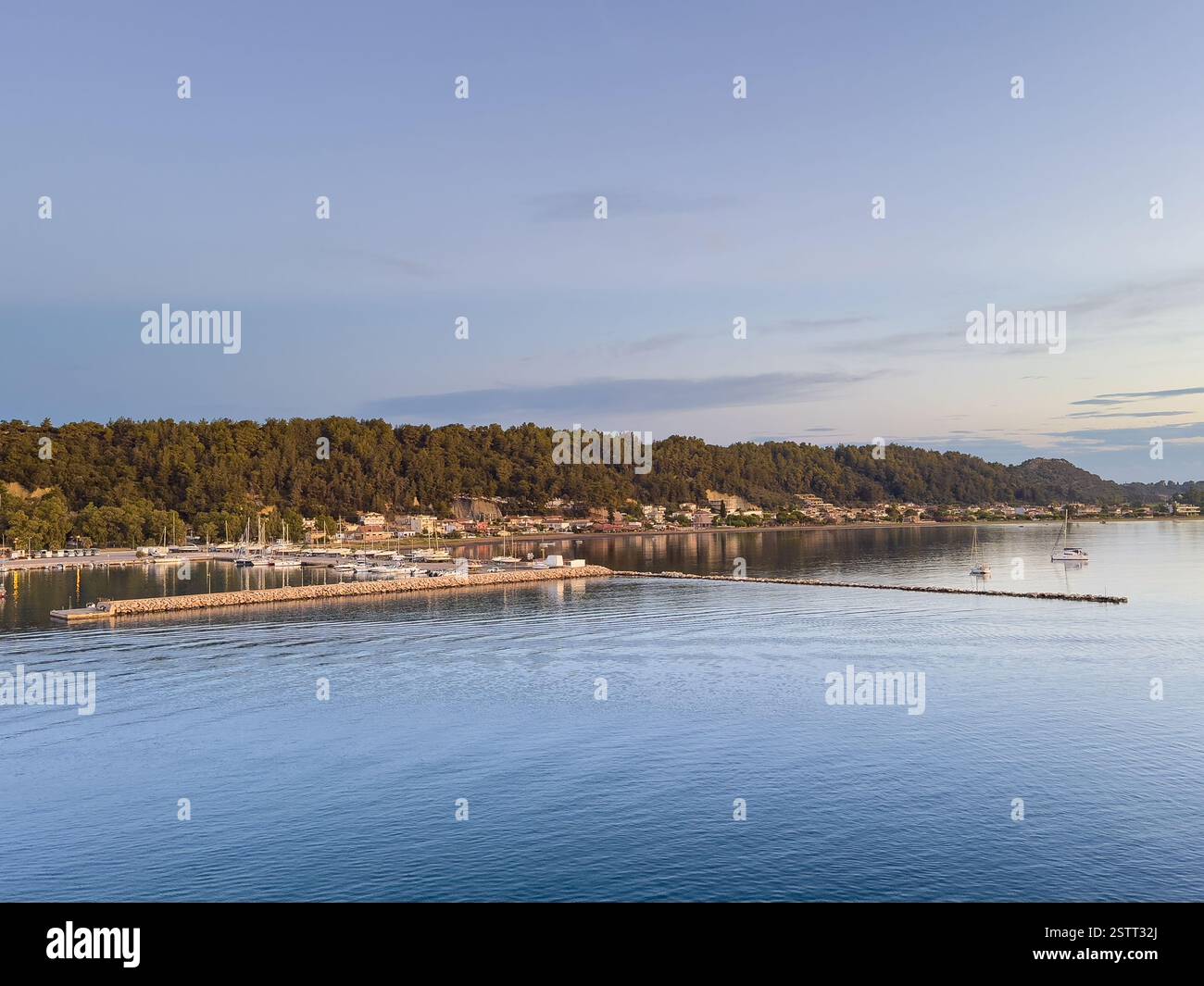 Katakolo, Grèce - 4 juillet 2024 : Katakolo Yacht Marina, Ilia, avec un littoral boisé derrière des bâtiments commerciaux le long de la promenade sous bleu clair Banque D'Images