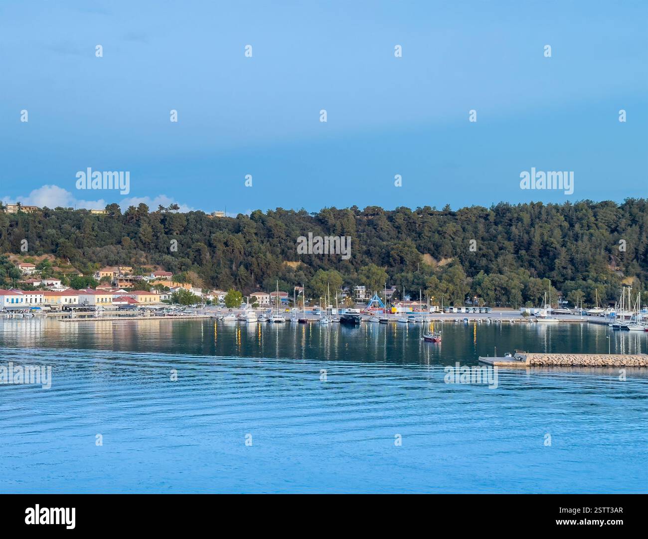 Katakolo, Grèce - 4 juillet 2024 : Katakolo Yacht Marina, Ilia, avec rivage boisé. Bâtiments commerciaux le long de la promenade sous le ciel bleu du matin Banque D'Images