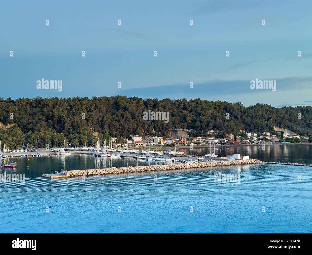 Katakolo, Grèce - 4 juillet 2024 : Katakolo Yacht Marina, Ilia, avec rivage boisé. Bâtiments commerciaux le long de la promenade sous le ciel bleu du matin Banque D'Images