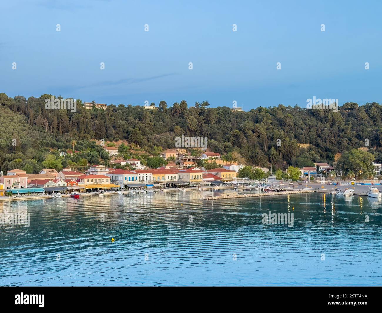 Katakolo, Grèce - 4 juillet 2024 : promenade le long de la ligne de spectacle du port de bâtiments commerciaux avec forêt sur la colline avec des manoirs saupoudrés à l'arrière. SMA Banque D'Images