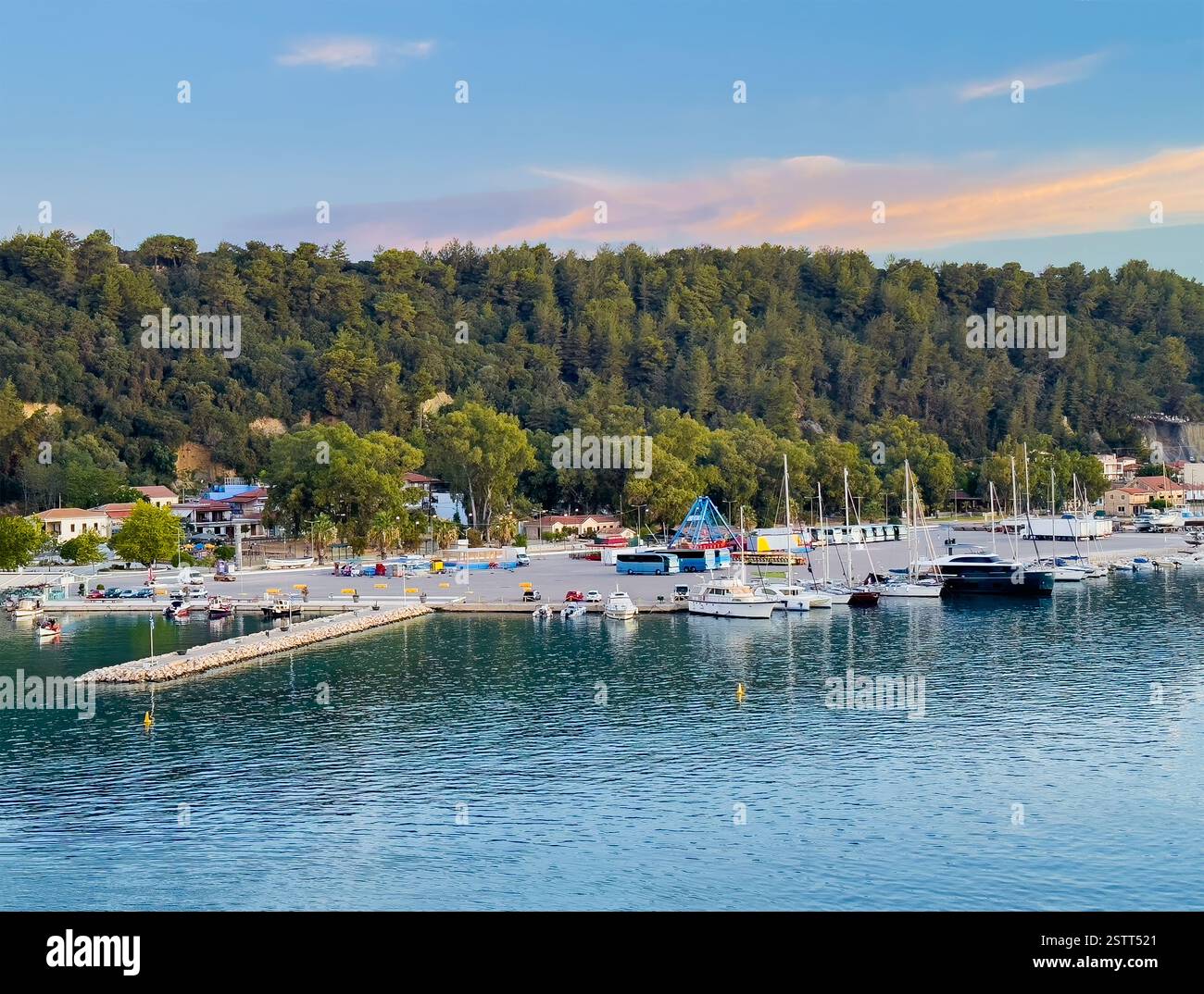 Katakolo, Grèce - 4 juillet 2024 : Katakolo Yacht Marina, Ilia, avec un littoral boisé derrière des bâtiments commerciaux le long de la promenade sous le morni bleu Banque D'Images