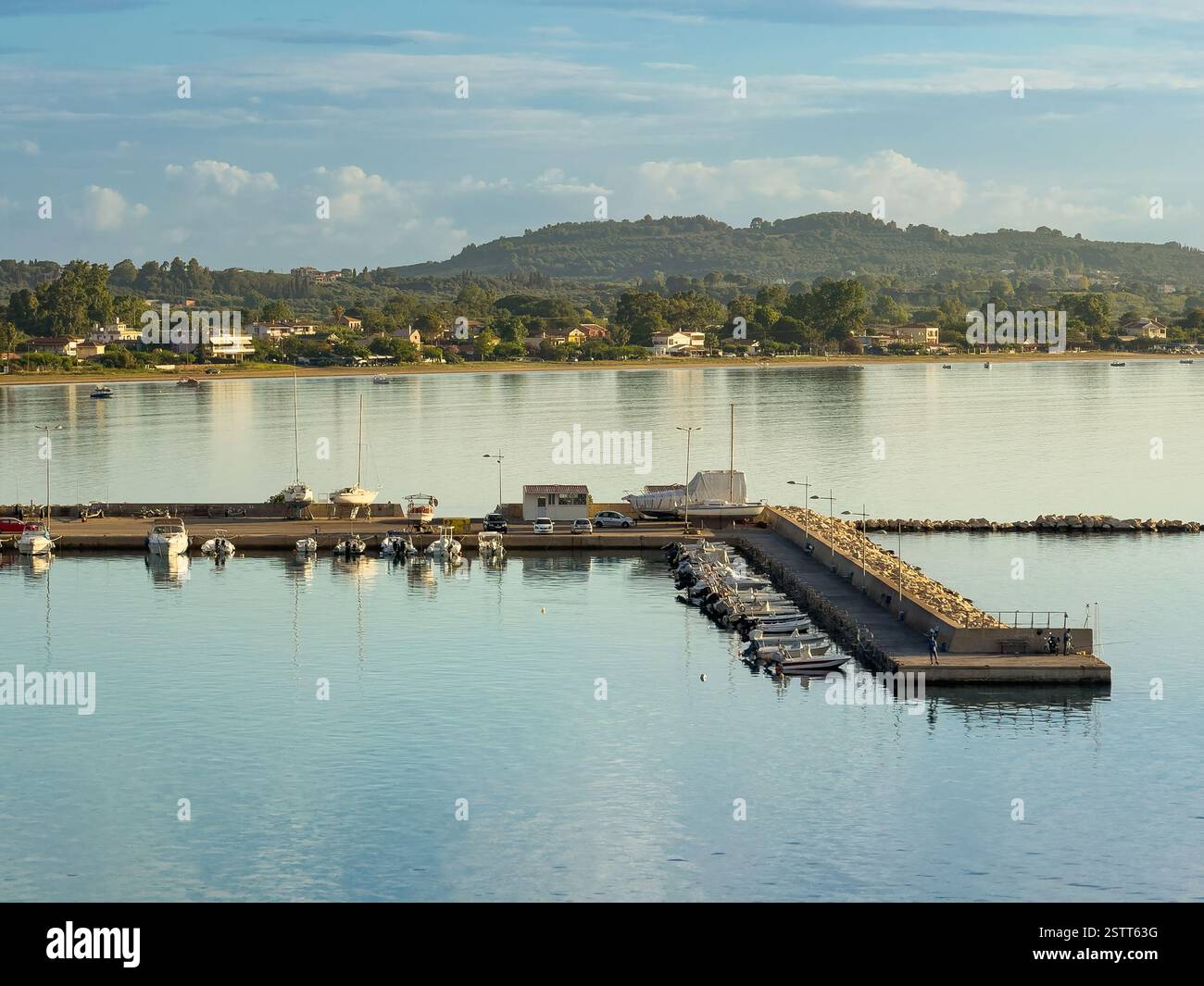 Katakolo, Grèce - 4 juillet 2024 : Katakolo Yacht Marina, Ilia, sous la lumière du matin. Ceinture de forêt verte sur le rivage avec quelques bâtiments modernes. Rangée de petits Banque D'Images