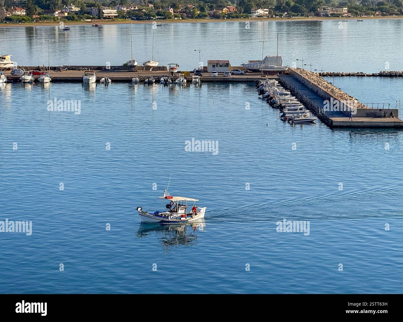 Katakolo, Grèce - 4 juillet 2024 : petit bateau de pêche revient à Katakolo Yacht Marina, Ilia. Jetées avec rangée de petits bateaux à moteur. Forêt verte b Banque D'Images