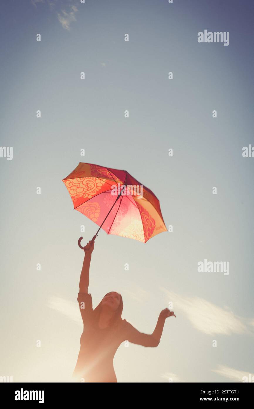La jeune fille danse avec des parapluies dans ses mains contre le ciel clair, l'image est teintée de couleurs rétro Banque D'Images