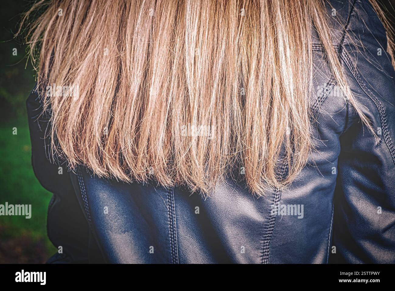 Longs cheveux blonds dispersés sur les épaules d'une jeune fille vêtue d'une veste en cuir noir Banque D'Images