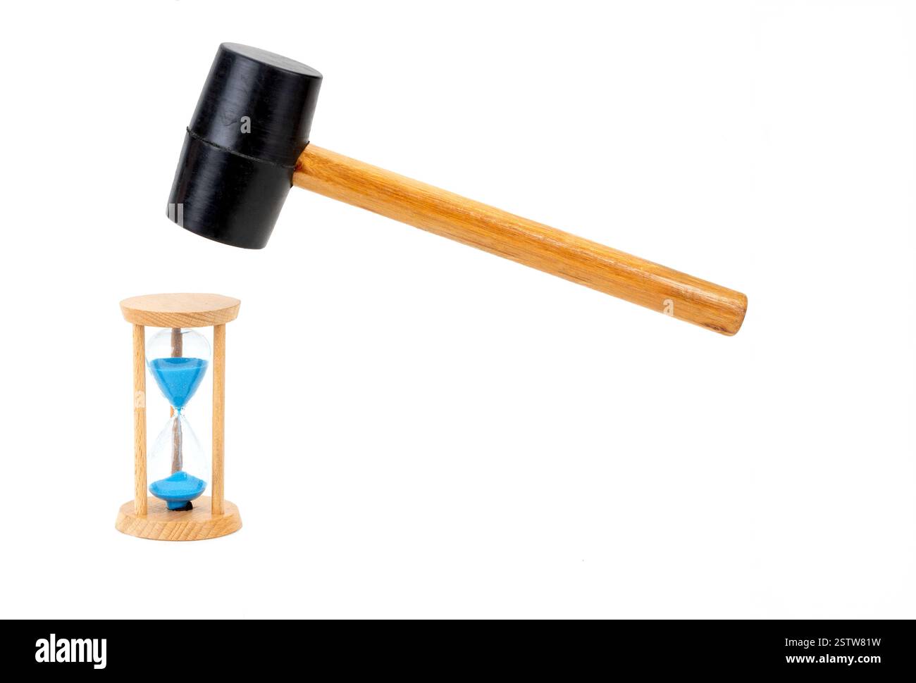 Le marteau en caoutchouc est sur le point de briser l'horloge en sablier sur fond blanc. Banque D'Images