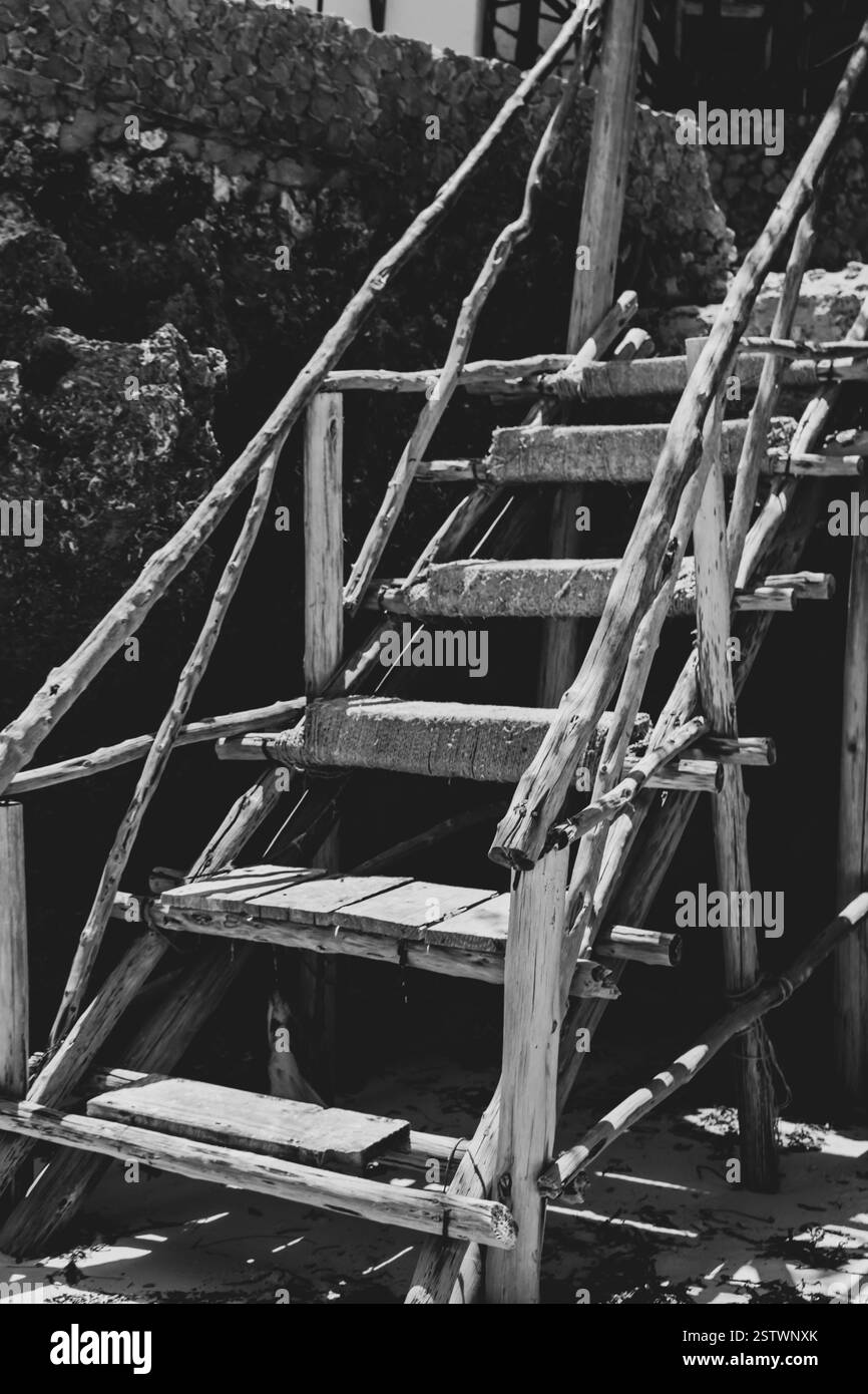 Vieil escalier en bois sur la plage. monochrome. Échelle rustique en pierres sur la plage tropicale, noir et blanc. Anciens escaliers sur le rocher. Banque D'Images