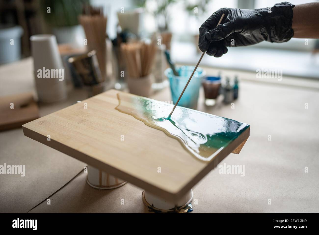 Paume de femme artistique, méticuleuse, attentive en gant noir travaillant sur la peinture en résine époxy. Banque D'Images