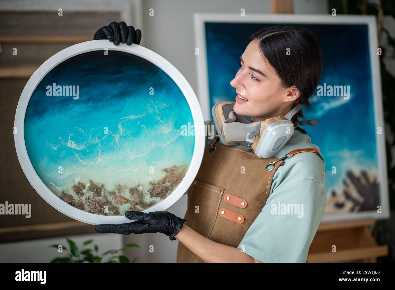 Femme artistique satisfaite regardant les œuvres d'art en résine époxy faites à la main faites dans la technique d'art fluide liquide. Banque D'Images