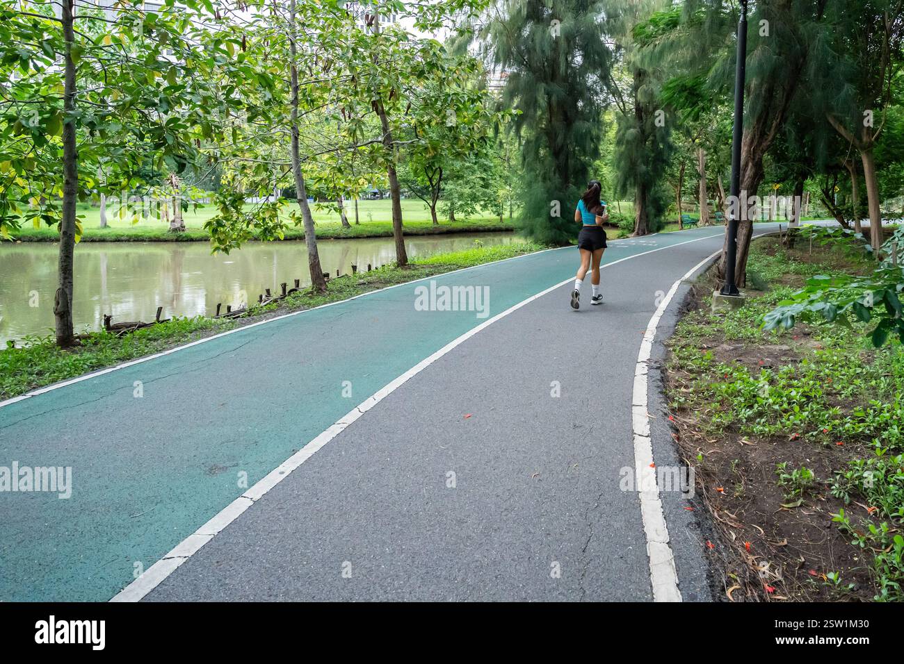 Jogging sur un sentier paisible du parc avec une végétation luxuriante et un plan d'eau Banque D'Images