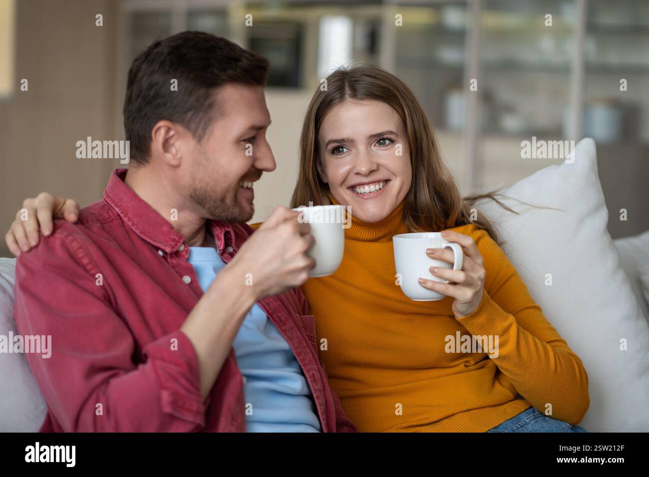 Couple amoureux femme homme passer le week-end paresseux boire un café assis sur le canapé à la maison, profiter de parler. Banque D'Images