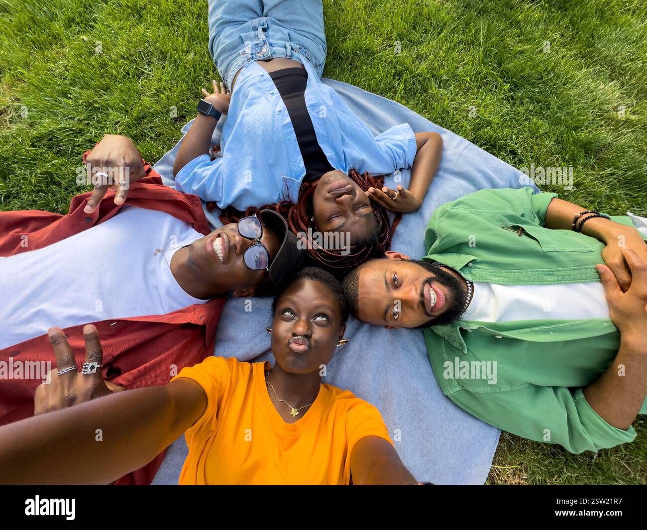 Groupe de quatre étudiants noirs amis goofing autour de l'herbe dans le parc, prenant des selfies tout en grimacant Banque D'Images