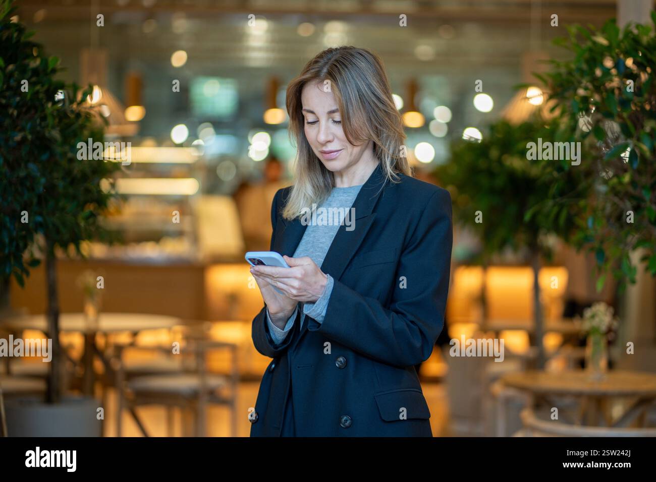 Femme d'affaires souriante à l'aide d'un smartphone, en tapant un message textuel, debout au restaurant de café. Banque D'Images