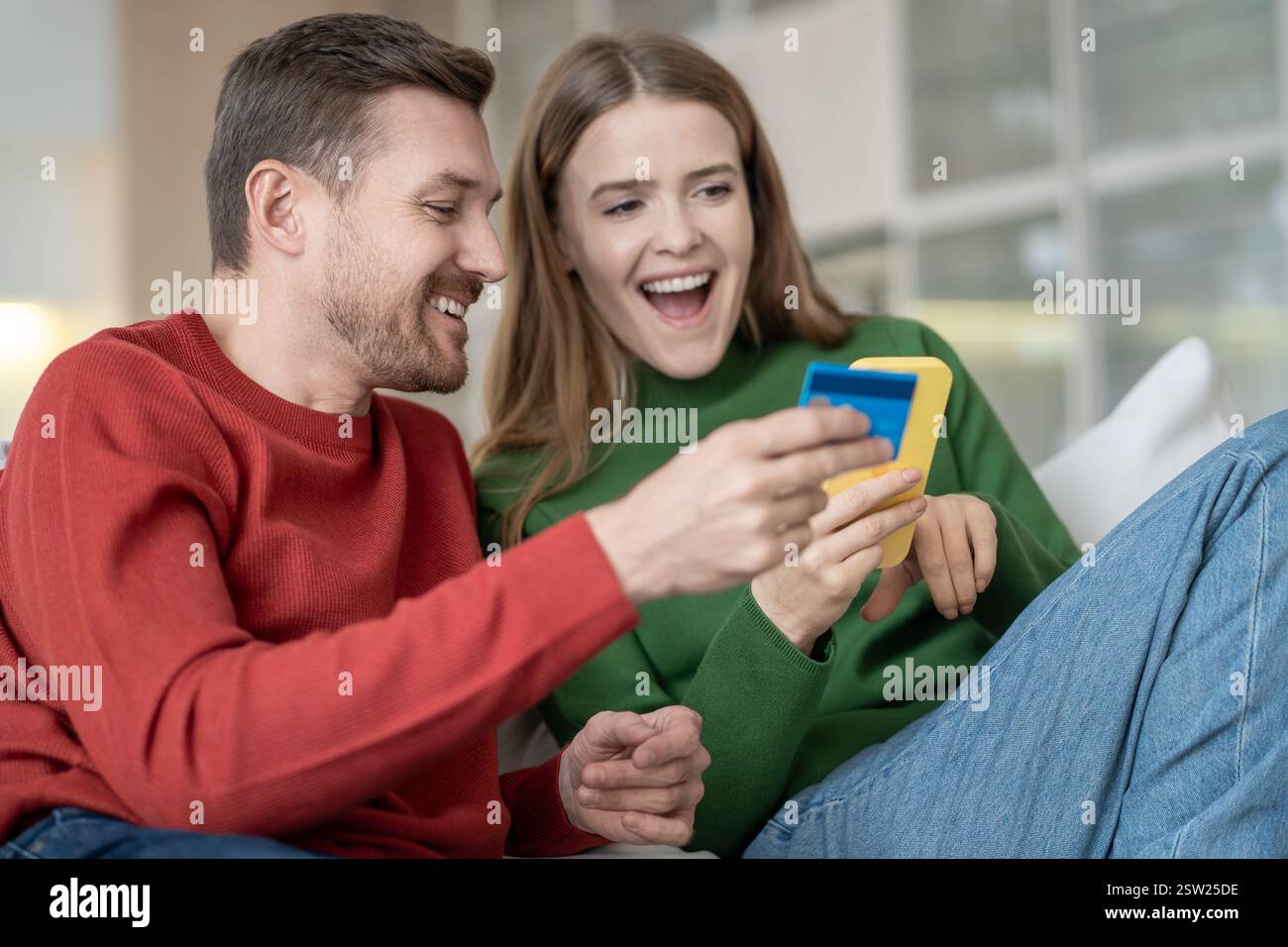 Heureux couple marié ravi utilisant le téléphone pour le shopping en ligne souriant payer par carte de crédit à la maison Banque D'Images
