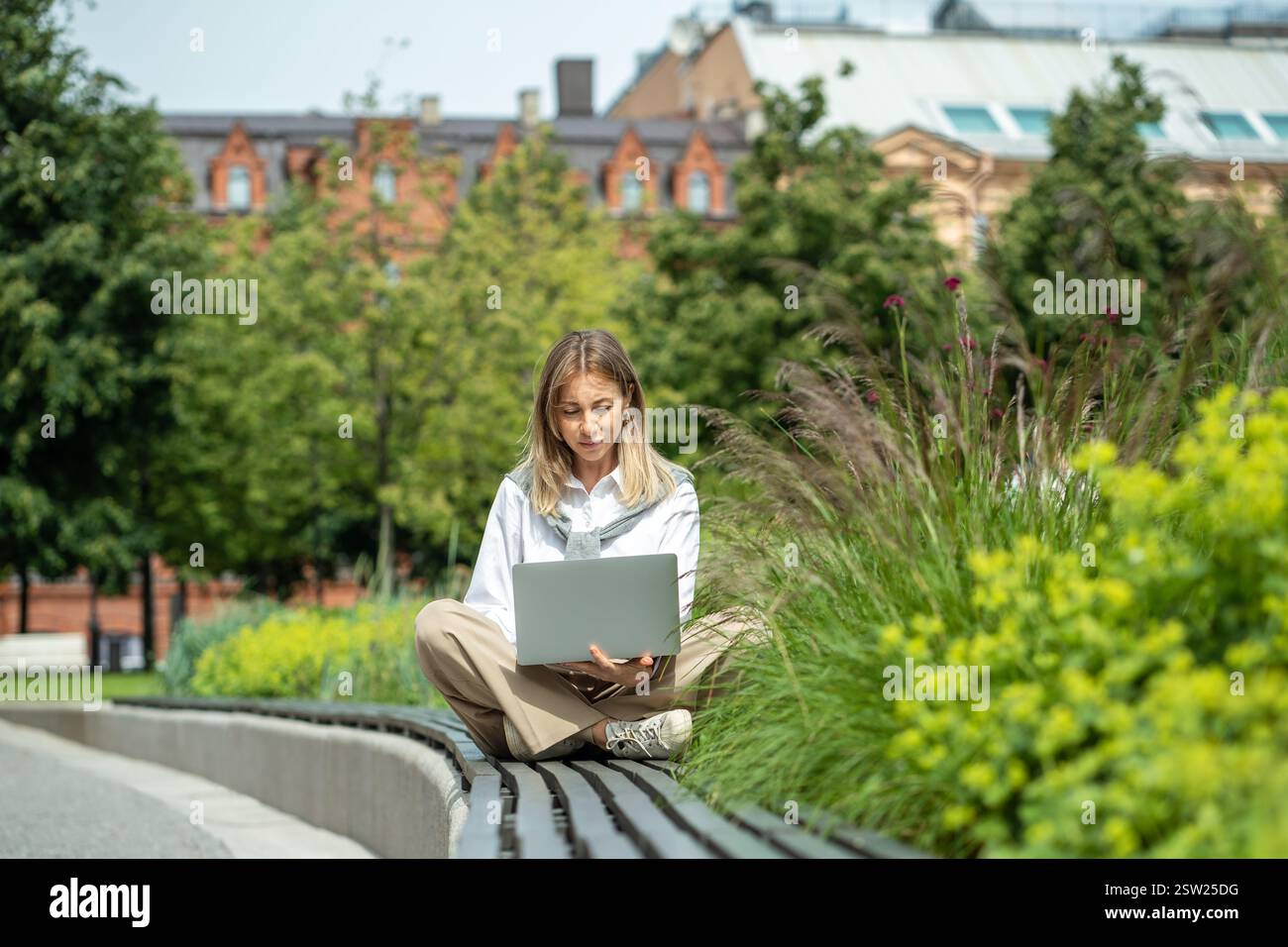 Jeune femme d'affaires travaillant à distance sur ordinateur portable dans le parc, apprécie l'espace de travail extérieur en tant que freelance Banque D'Images