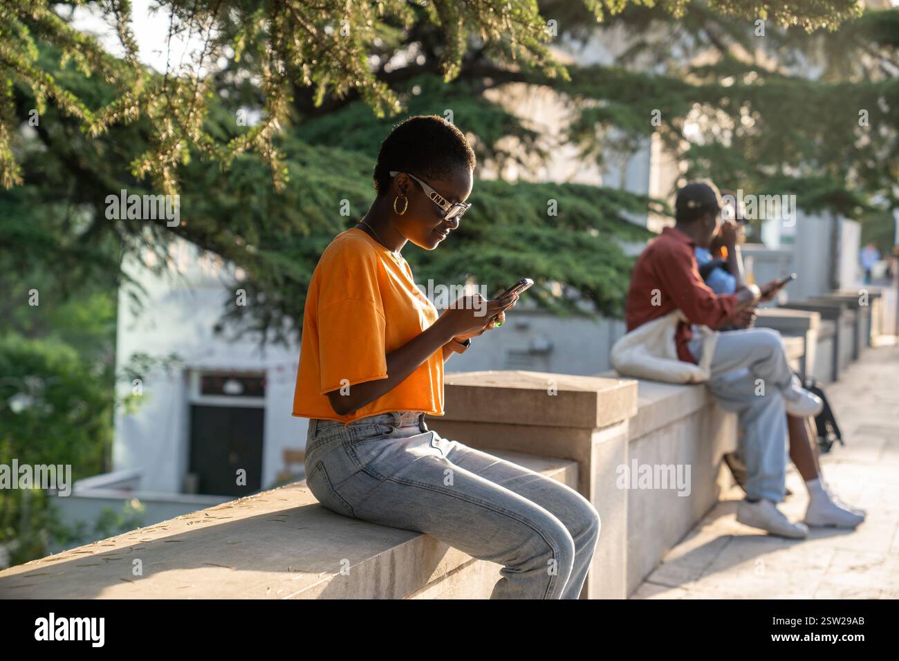 Heureuse femme afro-américaine optimiste avec smartphone à l'extérieur assis dans le parc par temps ensoleillé Banque D'Images