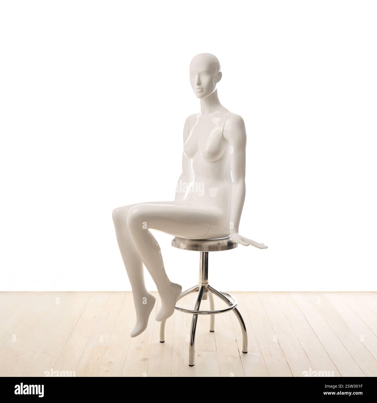 Mannequin féminin blanc assis est positionné élégamment sur un tabouret en métal sur un fond blanc avec un plancher en bois. Banque D'Images