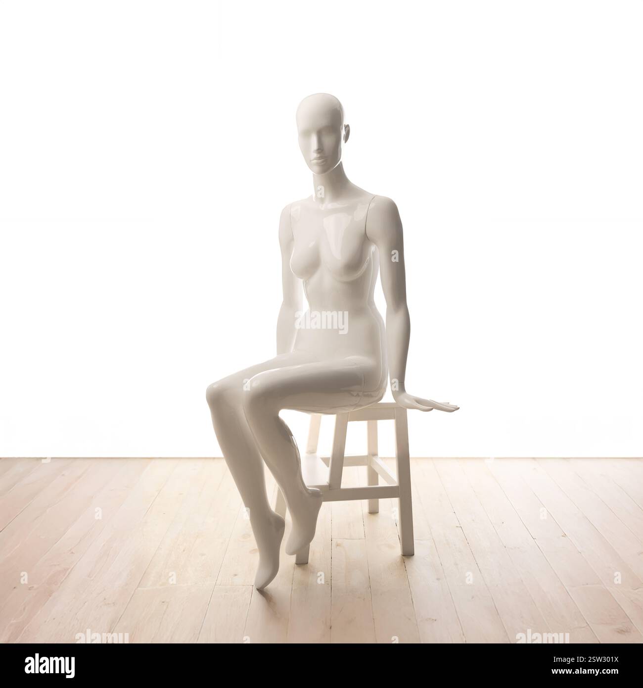 Mannequin féminin blanc assis est positionné élégamment sur un tabouret sur un fond blanc avec un plancher en bois. Banque D'Images