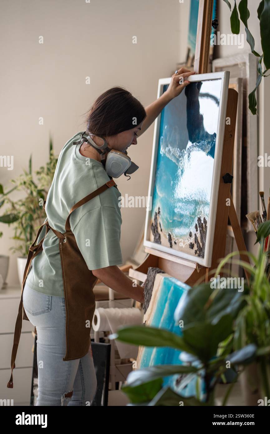 Femme artistique focalisée mettant la toile avec la peinture de résine époxy dans la technique d'art liquide sur chevalet. Banque D'Images