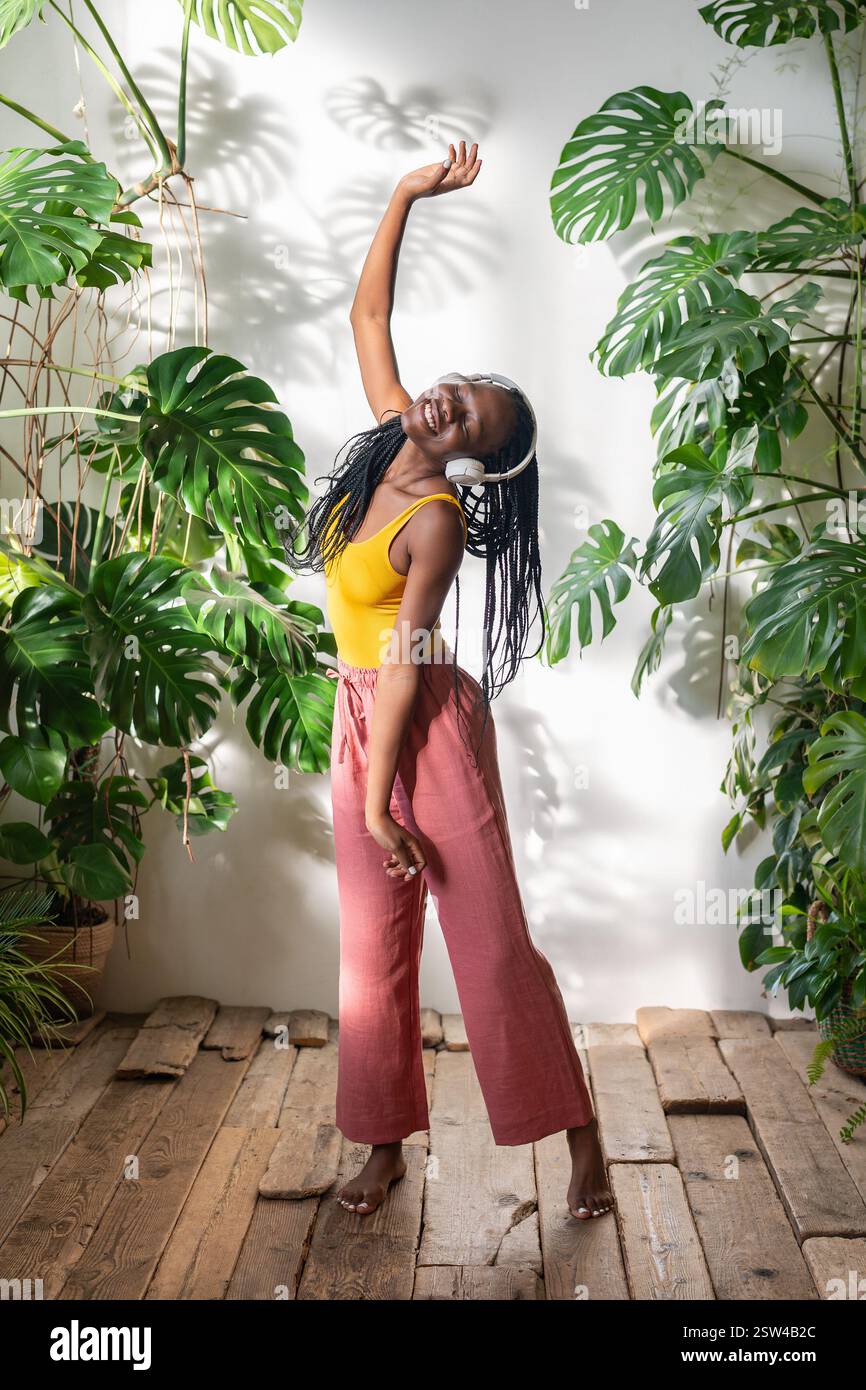 Positive fille noire dansant pieds nus sur plancher en bois dans des écouteurs écoutant de la musique profitez du moment. Banque D'Images