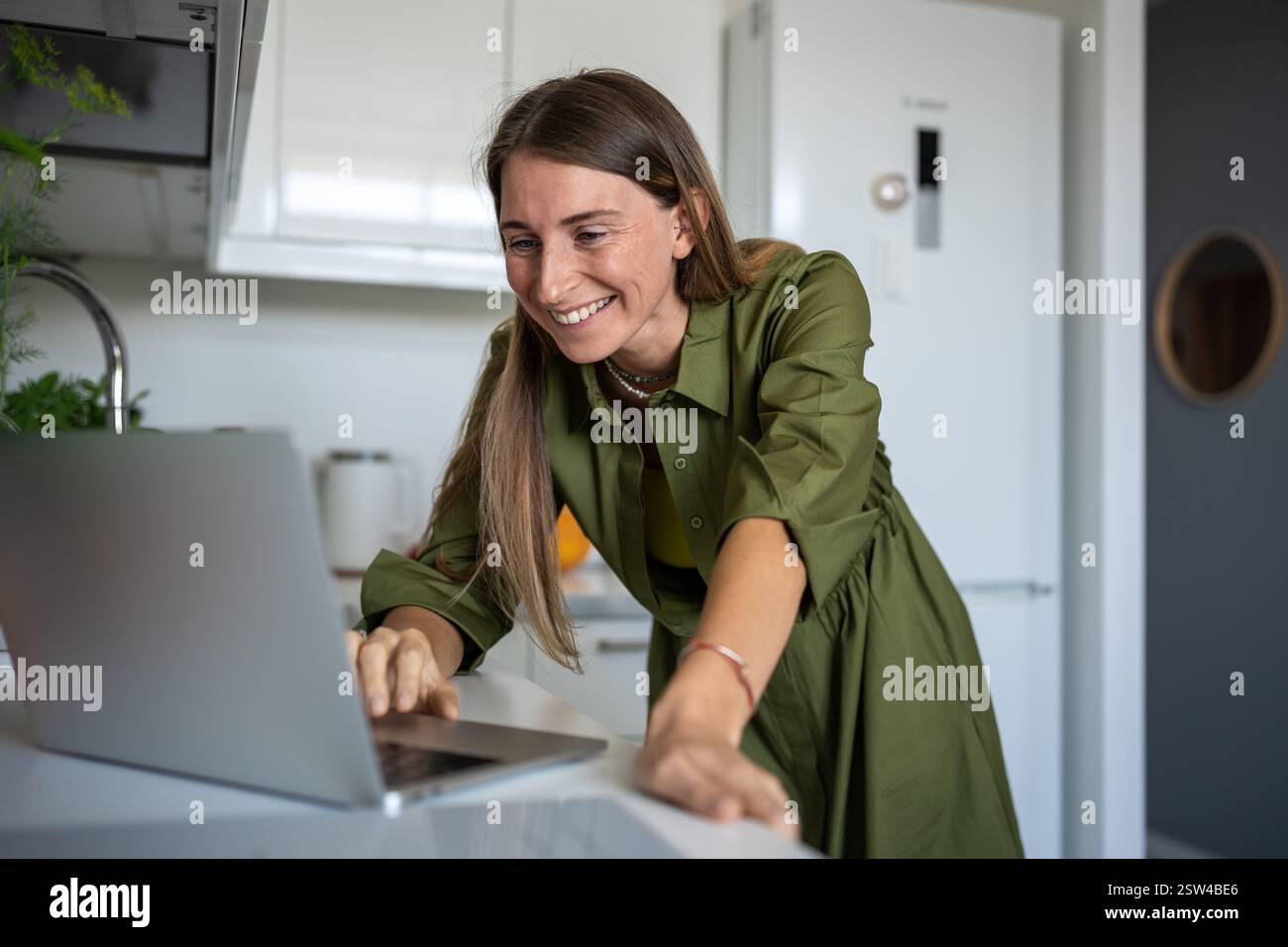 Femme heureuse avec le sourire à l'aide d'un ordinateur portable pour l'Internet de communication à distance en ligne dans la cuisine à la maison. Banque D'Images