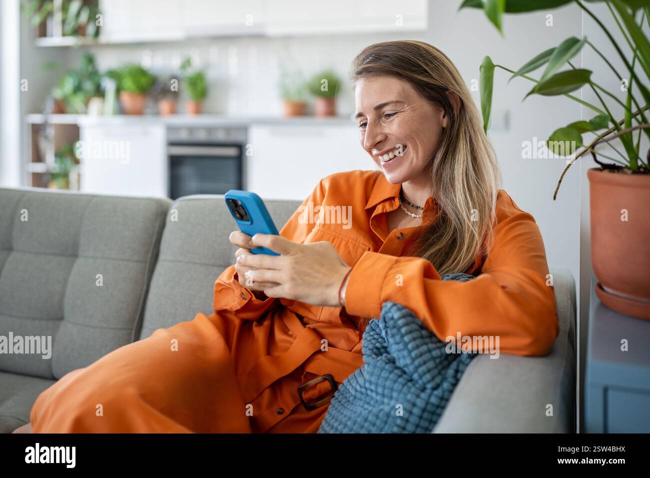 Femme suédoise heureuse à l'aide d'un smartphone, se reposant sur un canapé à la maison confortable et faisant défiler les réseaux sociaux Banque D'Images