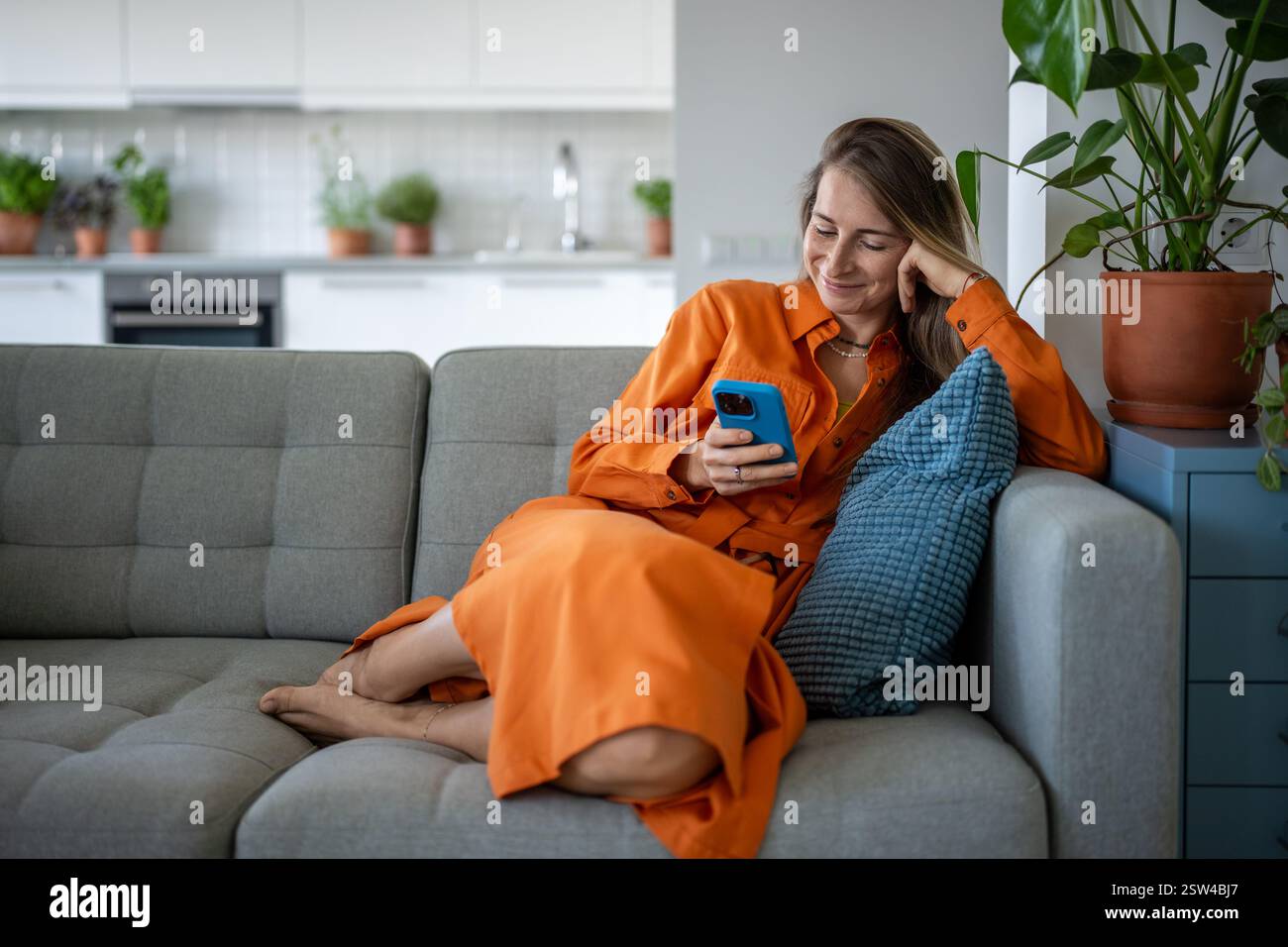 Femme heureuse utilisant un téléphone portable au canapé de la maison. Heureuse femme détendue avoir du plaisir sur Internet, discuter en ligne. Banque D'Images