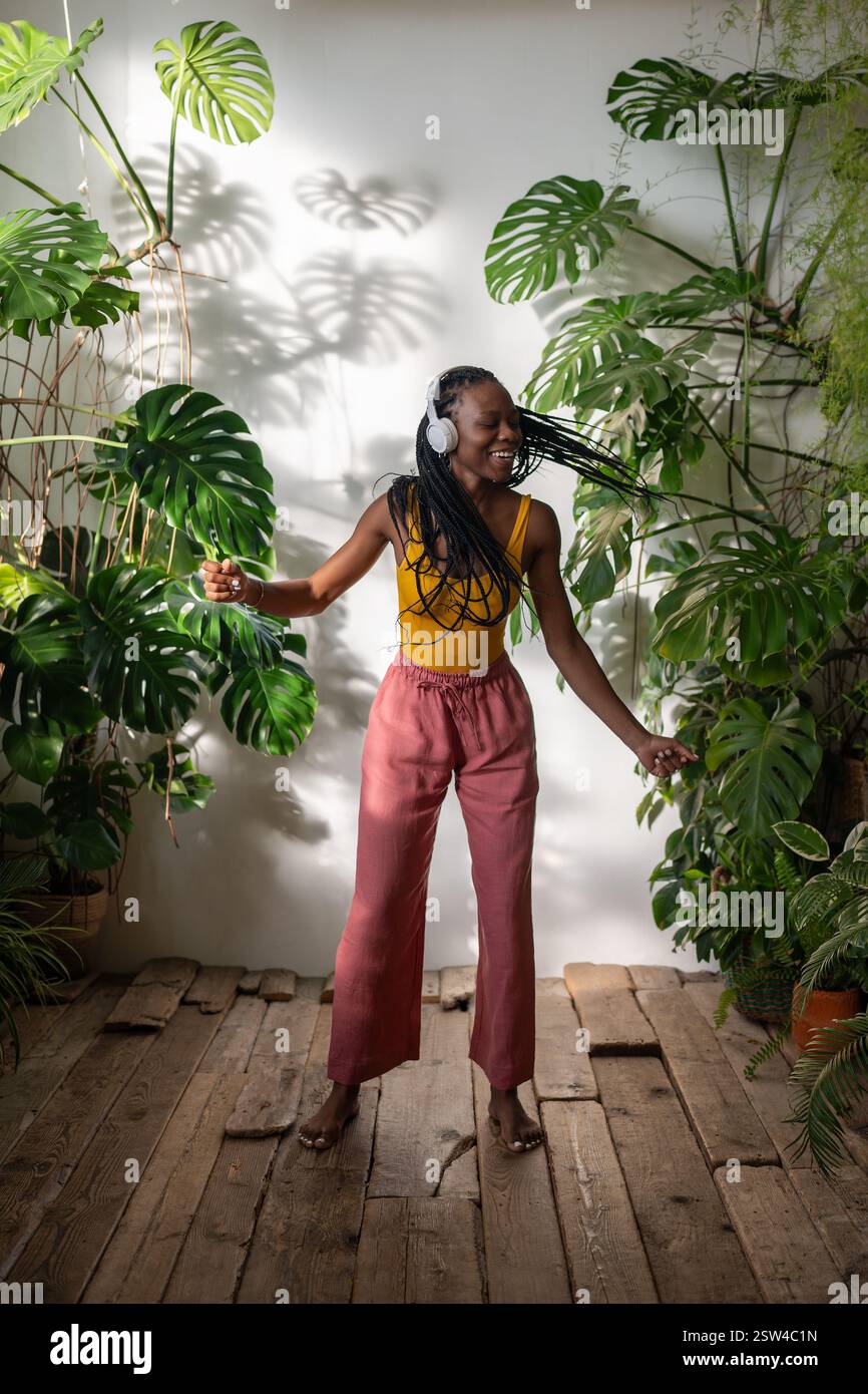 Positive fille noire dansant pieds nus sur plancher en bois dans des écouteurs écoutant de la musique profitez du moment. Banque D'Images
