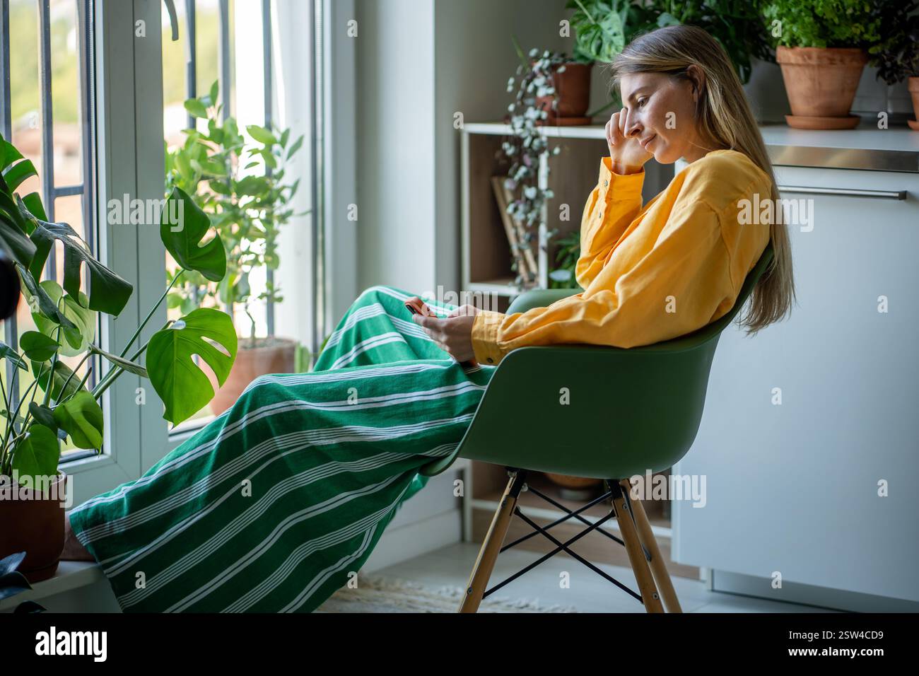 Femme fatiguée épuisée se relaxant après le travail, assise avec un téléphone portable, surfant sur Internet, messagerie Banque D'Images