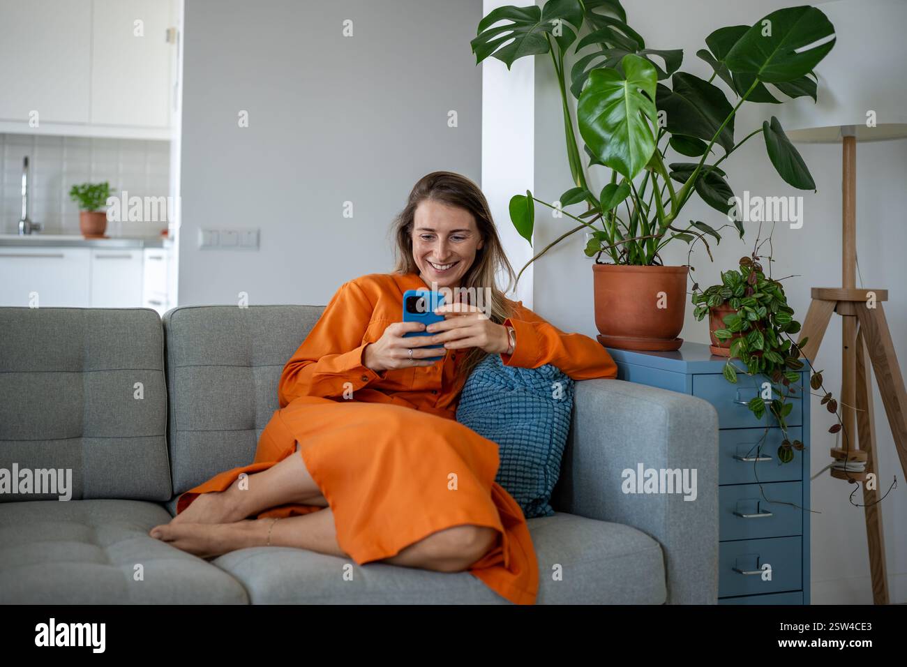 Femme heureuse utilisant un téléphone portable au canapé de la maison. Heureuse femme détendue avoir du plaisir sur Internet, discuter en ligne. Banque D'Images