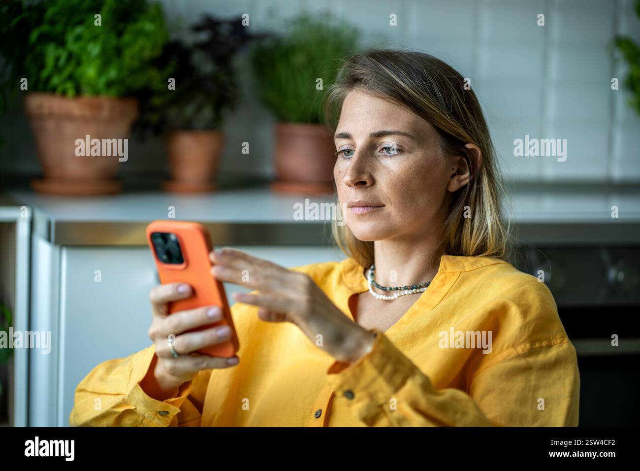 Réfléchie femme européenne détendue cherchant à filtrer le message de lecture de téléphone portable, le défilement du Web à la maison Banque D'Images