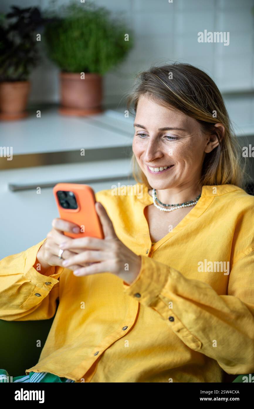 Femme heureuse avec le sourire cherchant à écran de défilement de téléphone portable passant le week-end détendu à la maison Banque D'Images