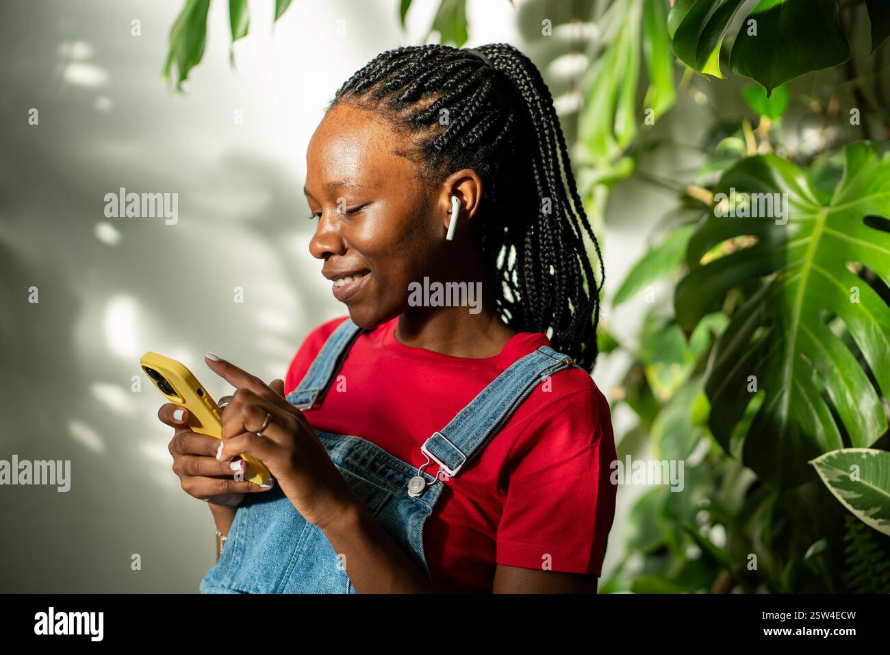 Femme noire détendue dans des écouteurs à l'aide d'un smartphone à la maison, sélectionne la piste de musique préférée dans l'application. Banque D'Images