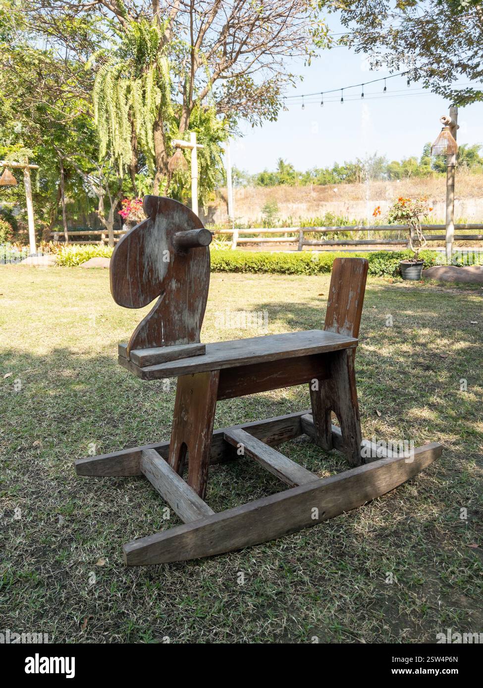 Un cheval à bascule en bois rustique se trouve dans le jardin paisible d'un petit café, entouré d'une végétation luxuriante et d'une atmosphère extérieure sereine, vue de face pour Banque D'Images