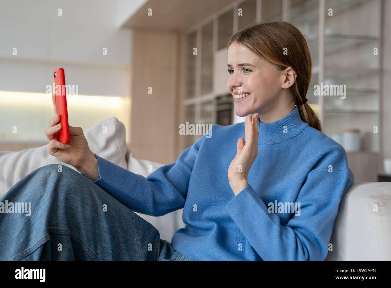Femme heureuse faire un appel vidéo agréable avec smartphone assis sur le canapé à la maison souriant regardant l'écran Banque D'Images