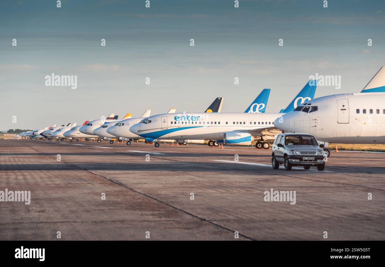SUV gris conduisant le long de nombreux avions garés dans l'aéroport par un après-midi ensoleillé. Vue latérale de dizaines d'avions de passagers placés en rangée. Banque D'Images