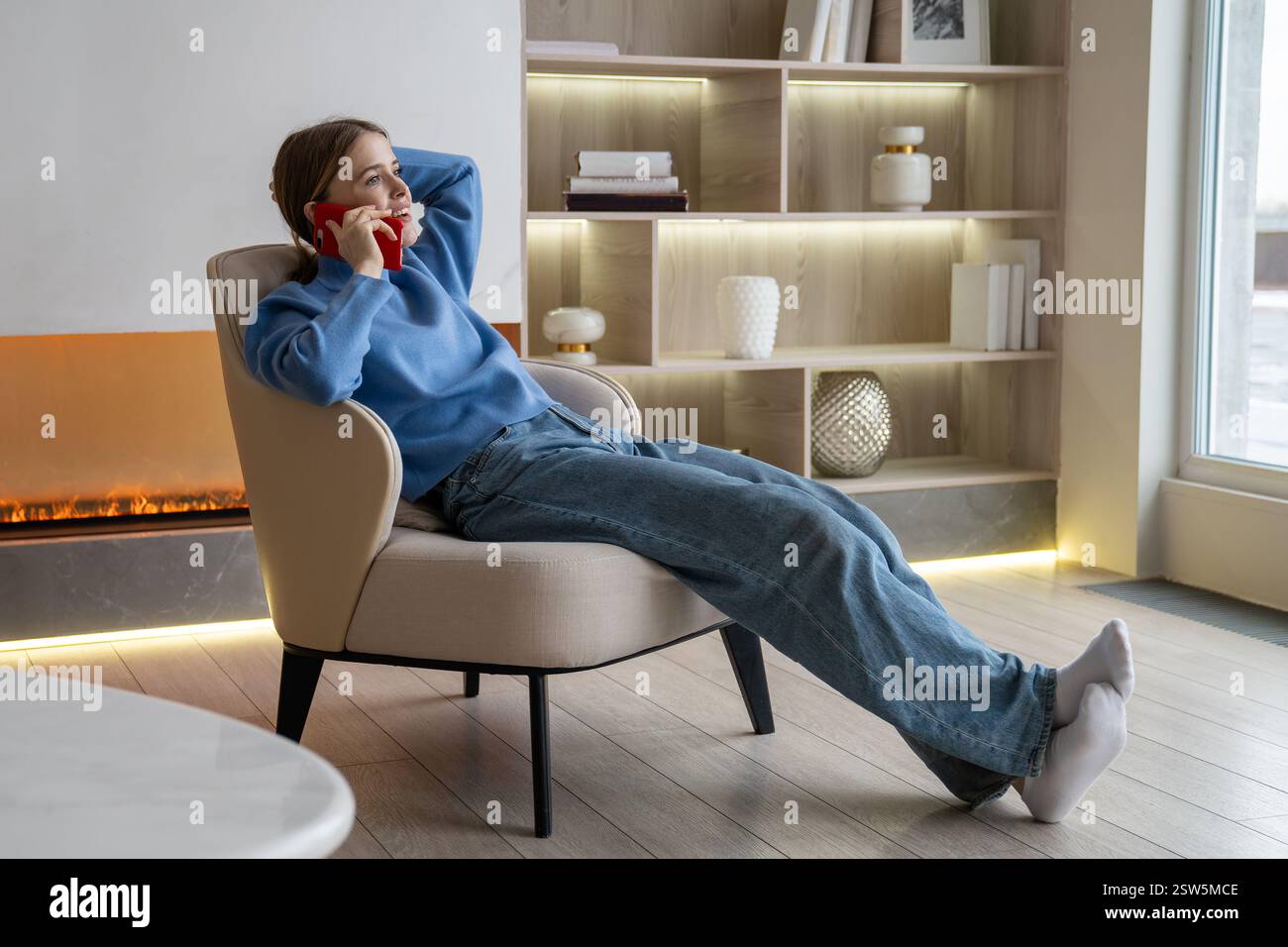 Fille détendue faisant des appels téléphoniques se reposer sur un fauteuil dans un appartement moderne confortable souriant profiter de la conversation Banque D'Images