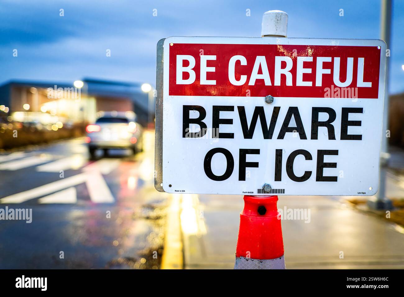Un panneau de sécurité routière est placé au bord d'une route au crépuscule avec le message d'avertissement « attention : attention à la glace ». Le panneau de mise en garde avertit les conducteurs et les piétons des conditions de glace potentiellement dangereuses sur la surface de la route. Le panneau est positionné de manière à être visible par la circulation en approche à mesure que la lumière du jour diminue, lorsque les dangers de glace peuvent devenir moins visibles. Banque D'Images