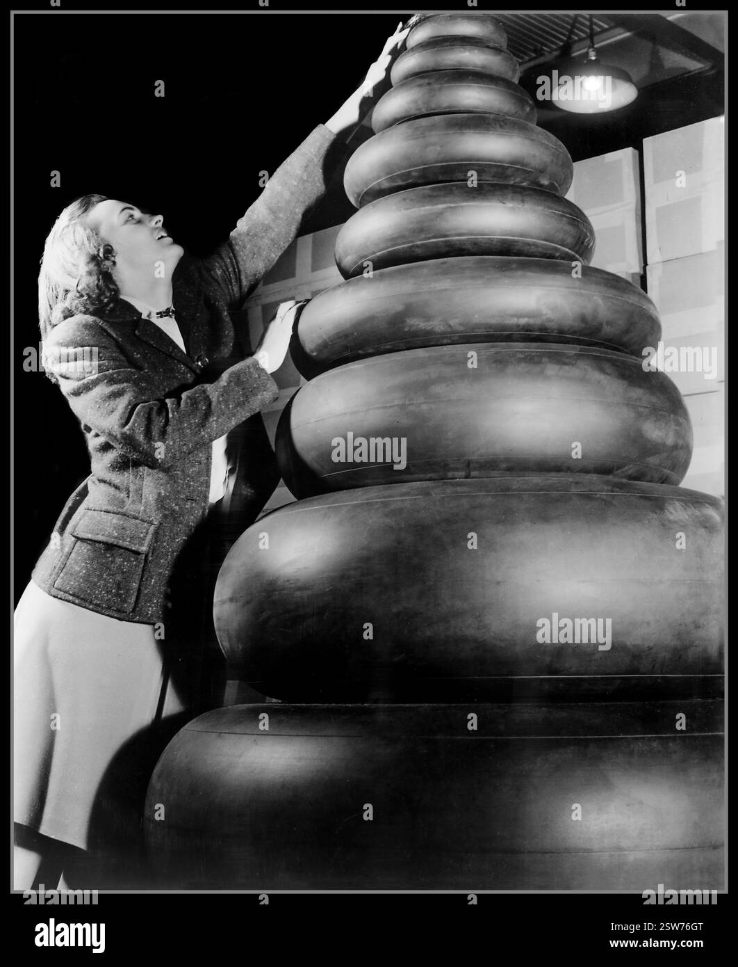 Les années 1940 WW2 femme vérificateur avec un large éventail de tailles de pneus en caoutchouc d'aviation militaire requises par les avions militaires de la seconde Guerre mondiale image de propagande pour l'effort de guerre aux États-Unis les motifs patriotiques ont constitué une grande partie des désirs des femmes d'entrer dans le travail de guerre. Les femmes dont les maris étaient en guerre étaient plus de deux fois plus susceptibles de chercher un emploi. Banque D'Images