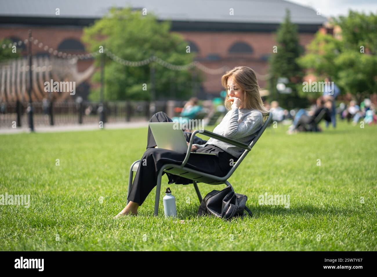 Femme de contenu dans le parc avec ordinateur portable et récipient de boisson isolé, gestion des appels, regarder des séries Banque D'Images