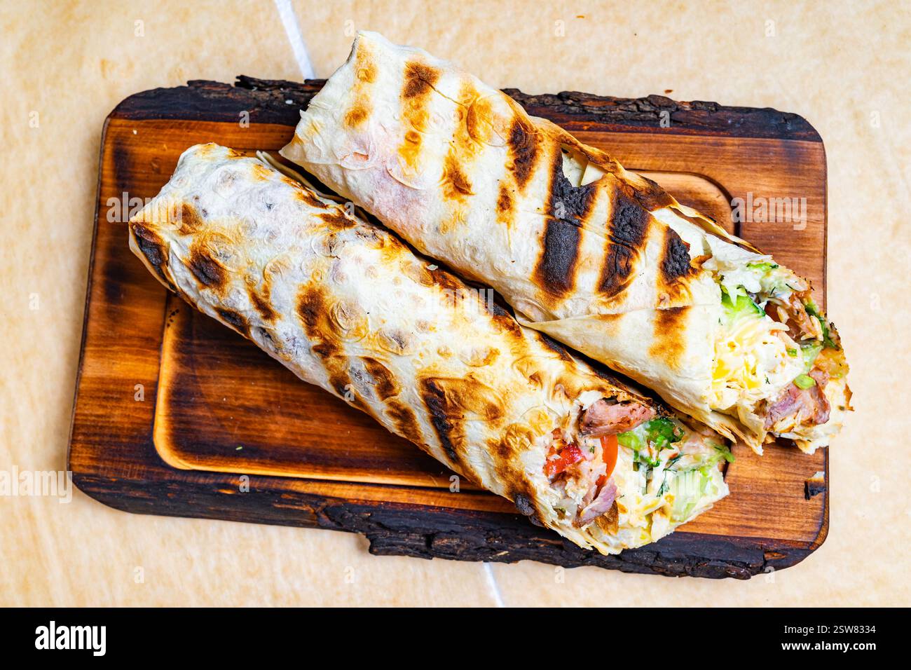 Deux wraps grillés remplis de légumes frais, de viandes et de sauces sont présentés sur une planche de bois. L'extérieur carbonisé suggère une saveur délicieuse, perf Banque D'Images