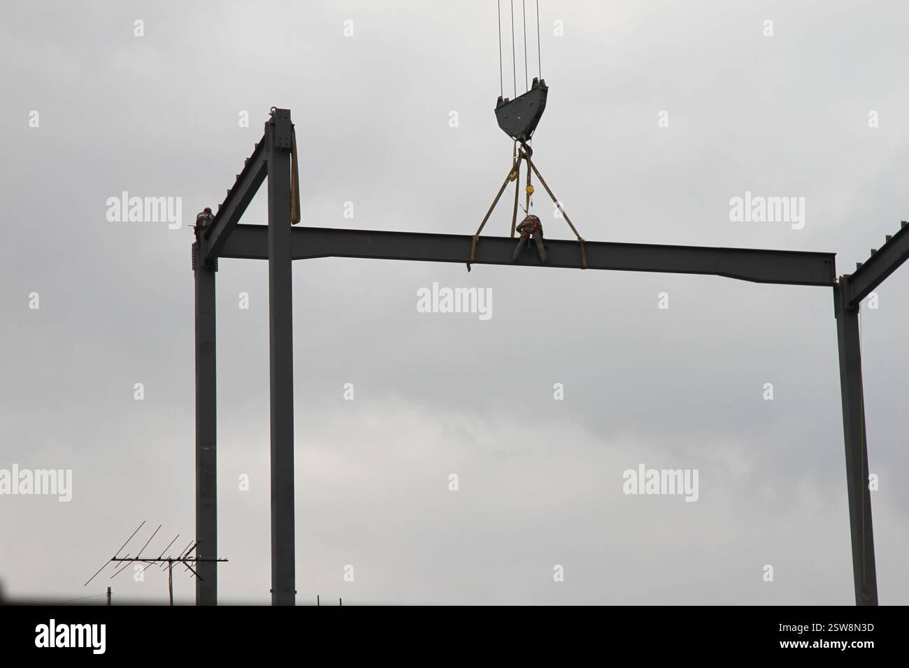 Un ouvrier de construction sur une poutre en acier dans les hauteurs pendant qu'il est transporté par une grue de construction. Un homme travaillant dans la construction. Banque D'Images
